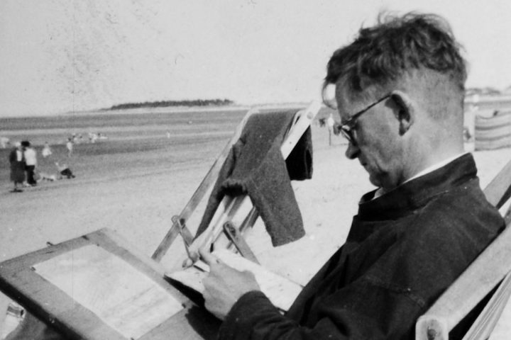 An image of a man drawing on a beach while sitting in a deckchair