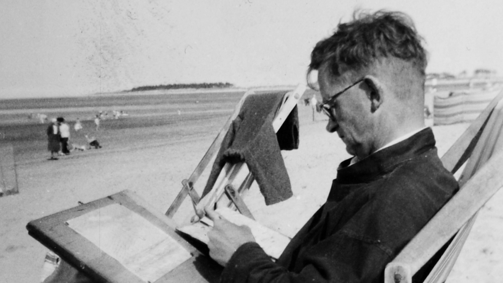 An image of a man drawing on a beach while sitting in a deckchair